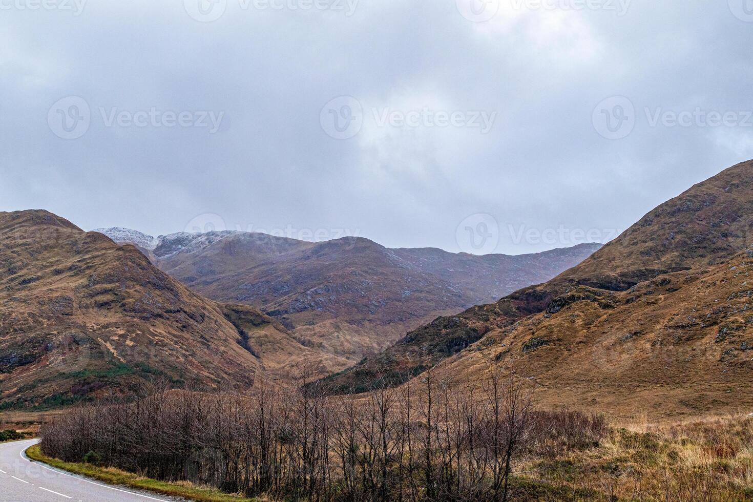 Scenic view of a winding road through a mountainous landscape with overcast skies in Scotland. photo