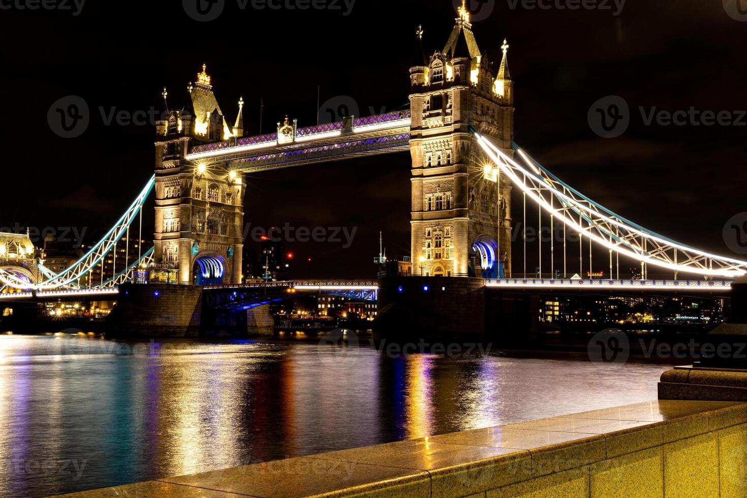 Night view of the illuminated Tower Bridge in London over the Thames River with reflections on water. photo