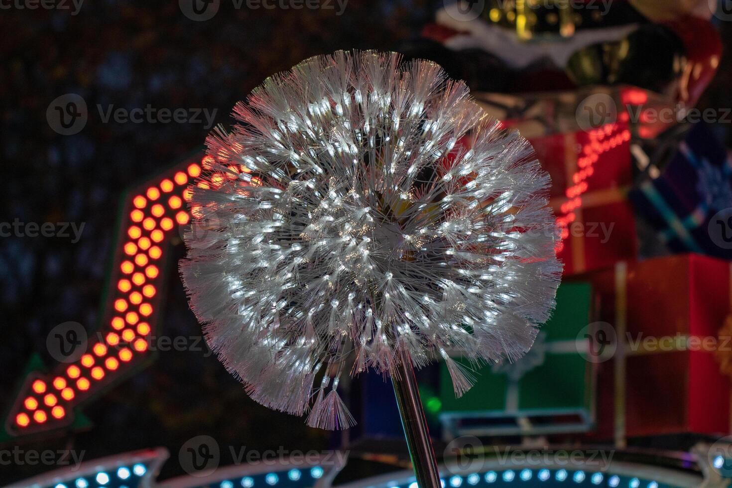 Illuminated dandelion-like light installation at night with blurred amusement park rides in the background. photo