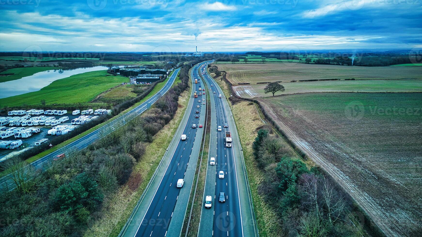 Aerial view of a busy highway with cars, surrounded by green fields and a cloudy sky. photo