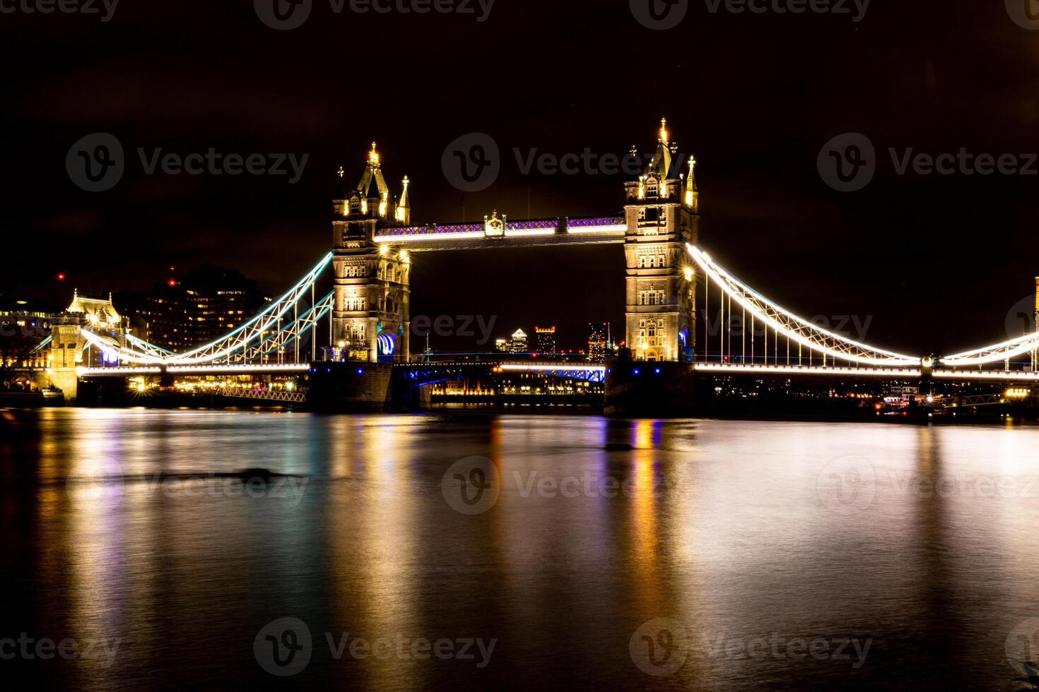 iluminado suspensión puente terminado río a noche con reflexiones en agua. foto