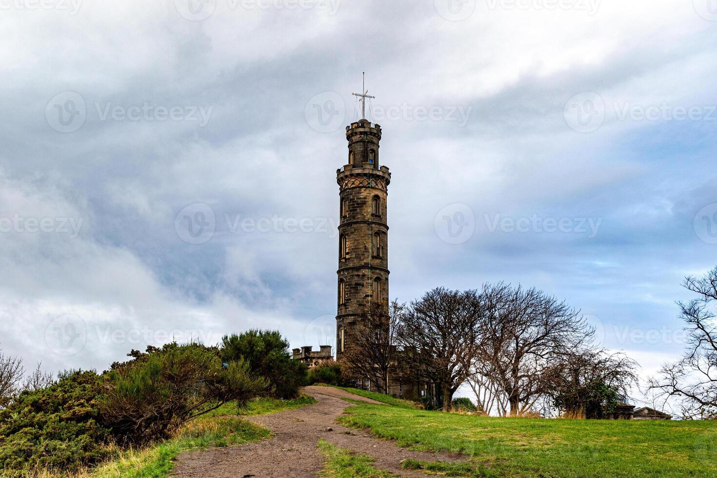 Historic stone tower on a hill with greenery under a cloudy sky. photo