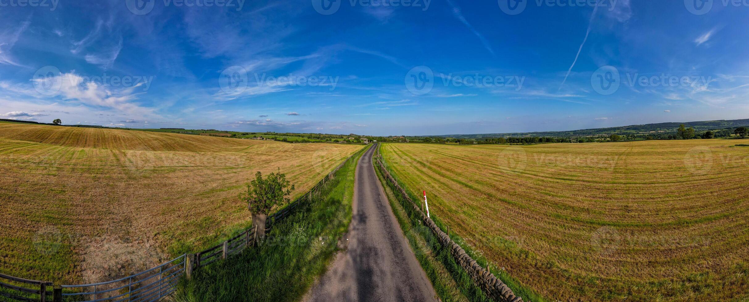 Panoramic view of a scenic country road cutting through golden fields under a vast blue sky with wispy clouds. photo