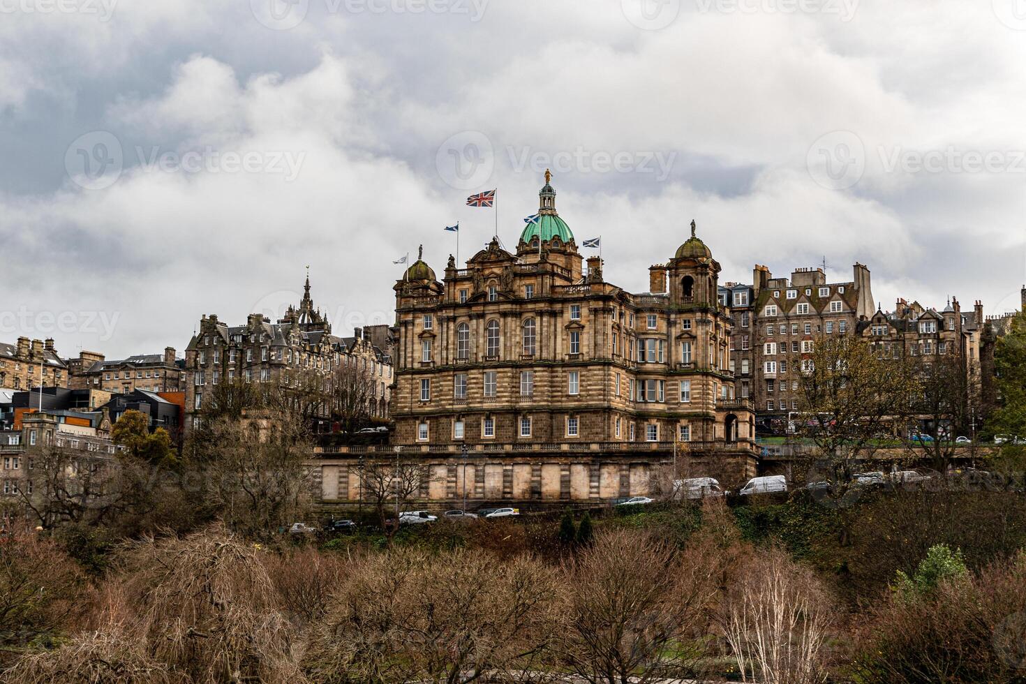 Historic building with copper domes amidst trees under a cloudy sky, Edinburgh. photo