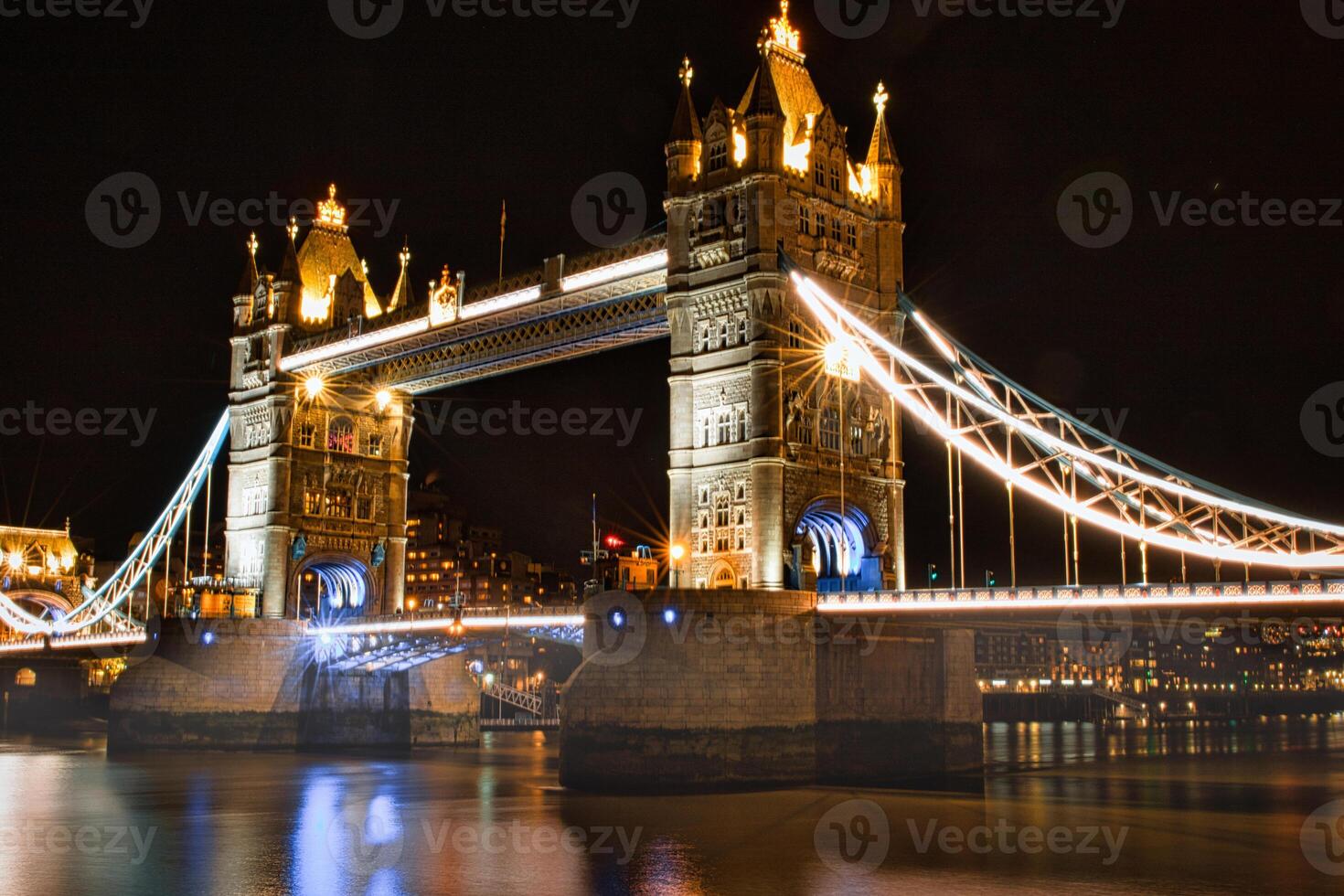Night view of Tower Bridge in London with illuminated lights reflecting on the Thames River. photo