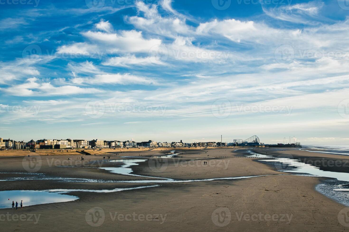 Serene beachscape with scattered pools of water, under a vast blue sky, with distant buildings lining the shore in Blackpool, England. photo