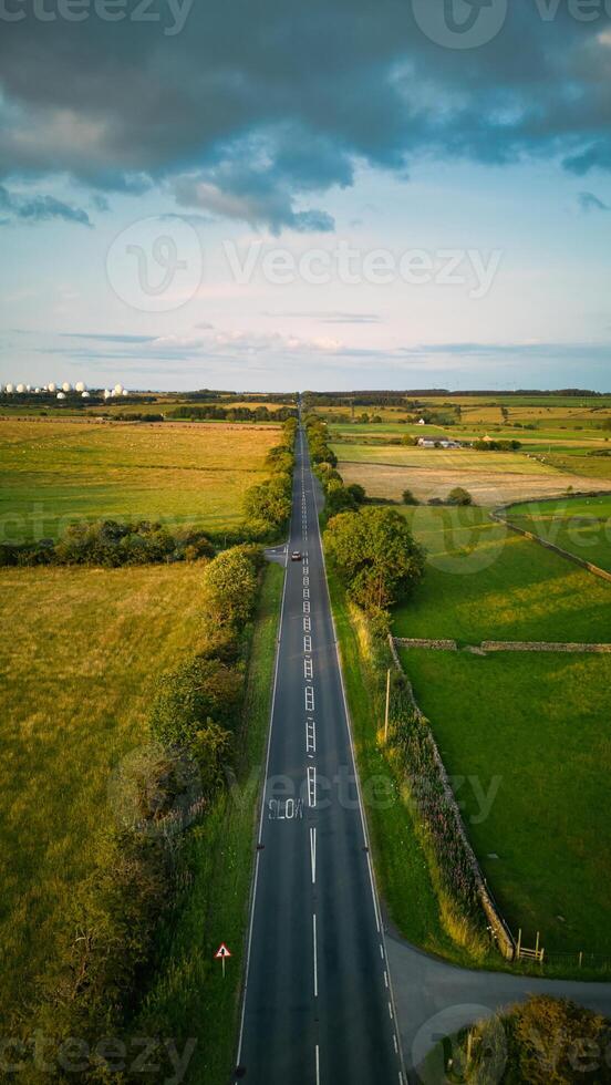Aerial view of a straight country road cutting through green fields with a cloudy sky above in Yorkshire. photo