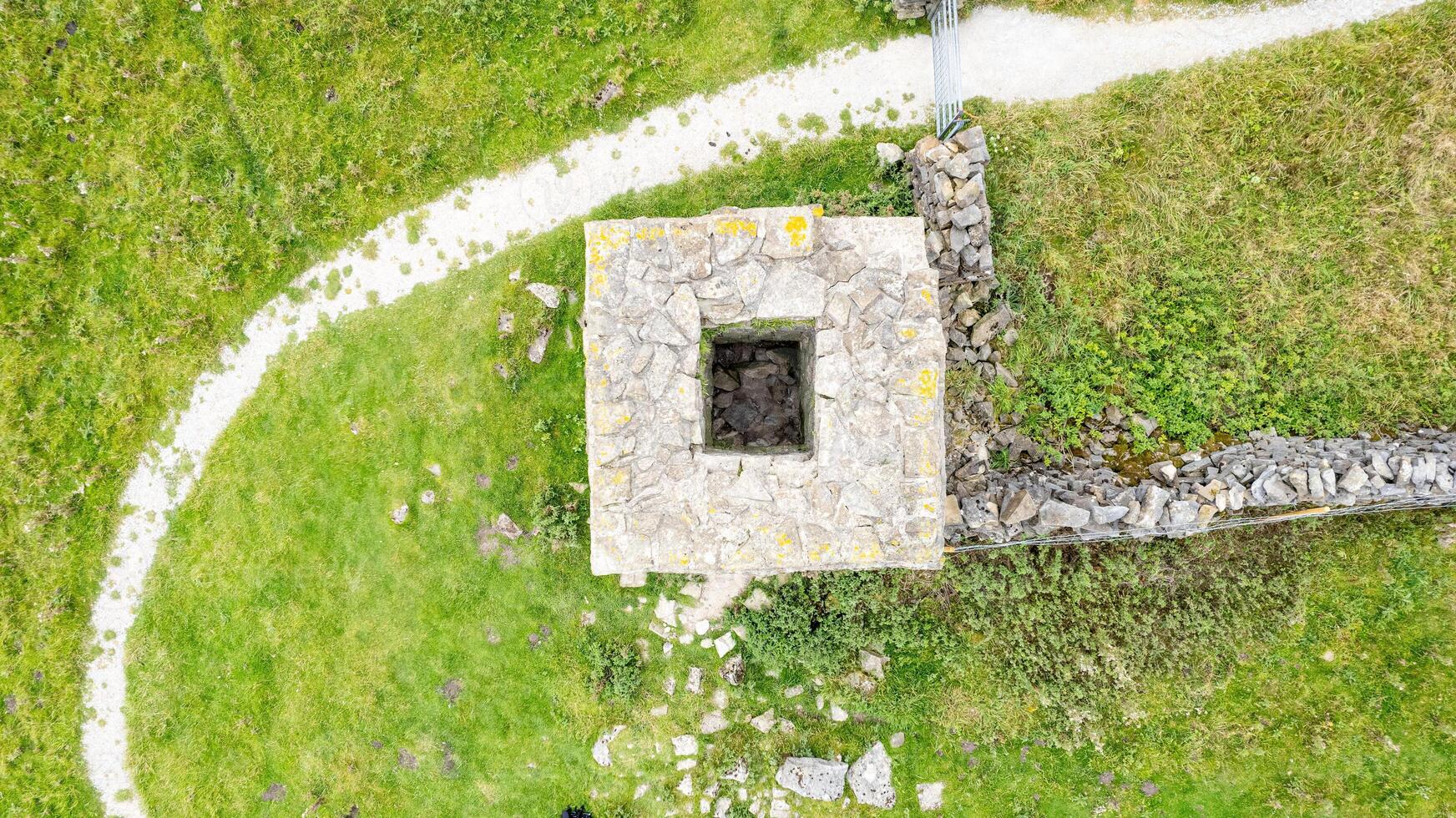 Aerial view of a small stone structure with a path in a green grassy field. photo