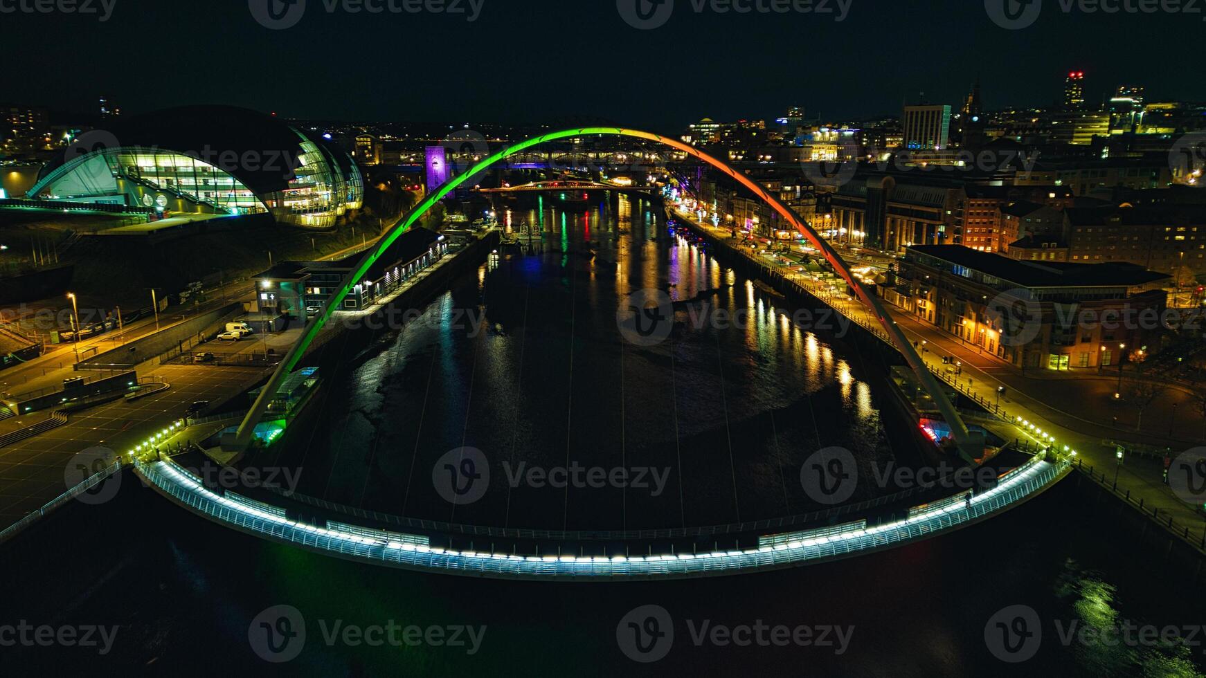 Night view of a cityscape with illuminated arched bridge over a river, reflecting colorful lights on water in Newcastle upon Tyne photo