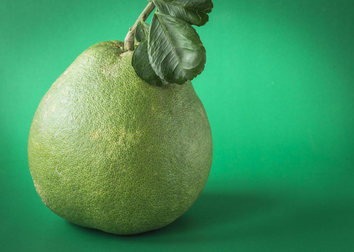 a green pomelo fruit with leaves on it photo