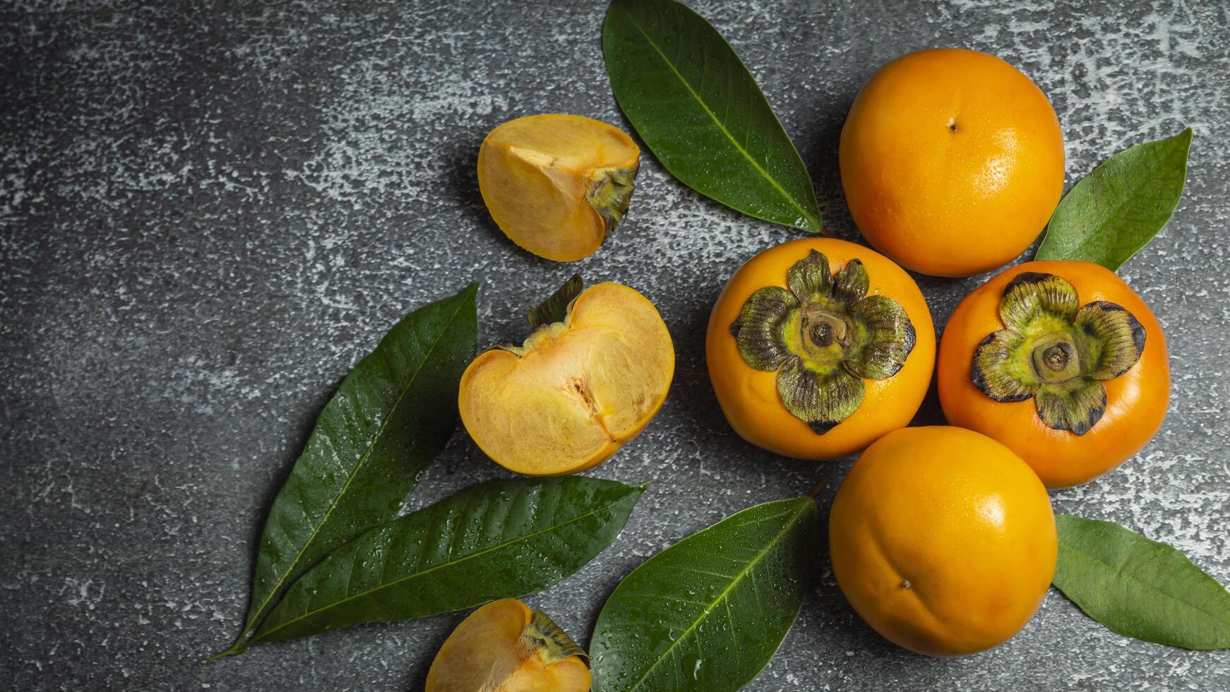 a bunch of persimmons with leaves on a gray surface photo