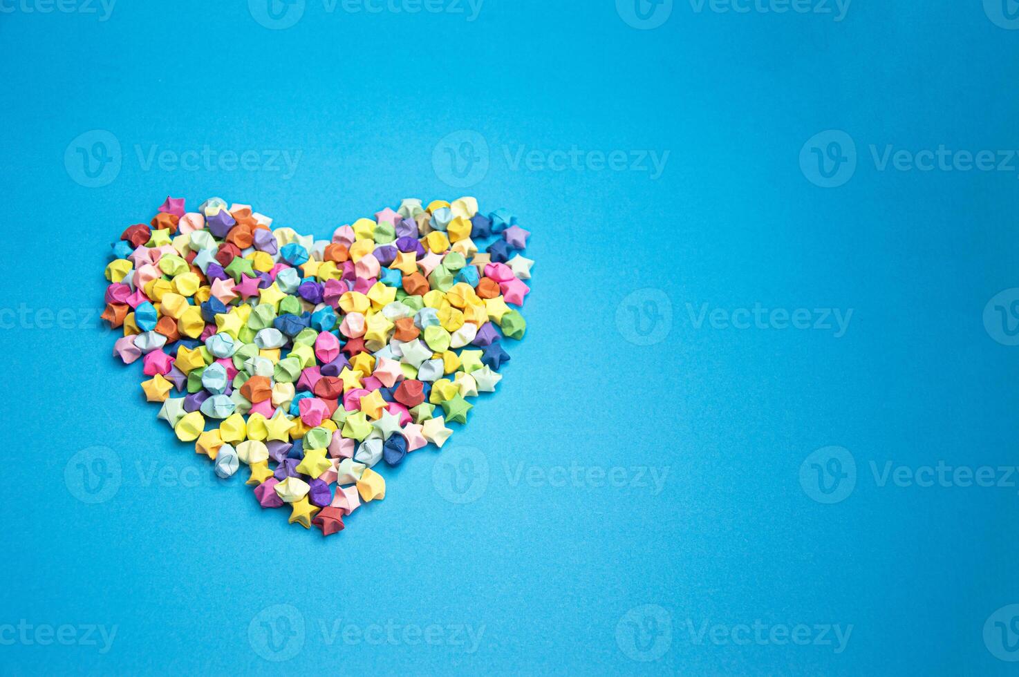 Paper folded into the shape of a multi-colored 5-pointed star, on a blue background. Arranged in the shape of a heart photo