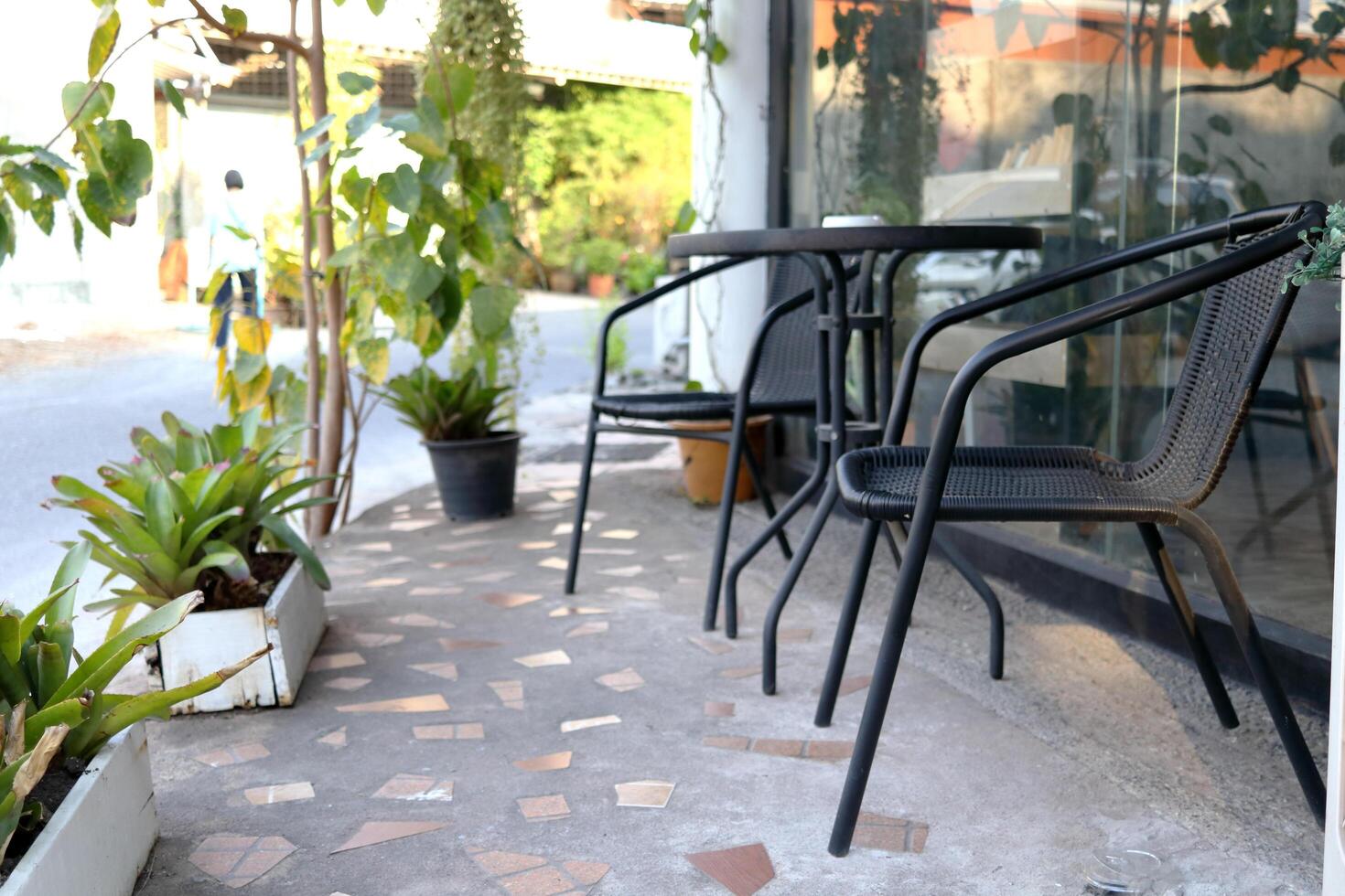 Black color set of metal chair and table on concrete floor outside coffee shop, white pot and plant decor beside, Thailand. photo