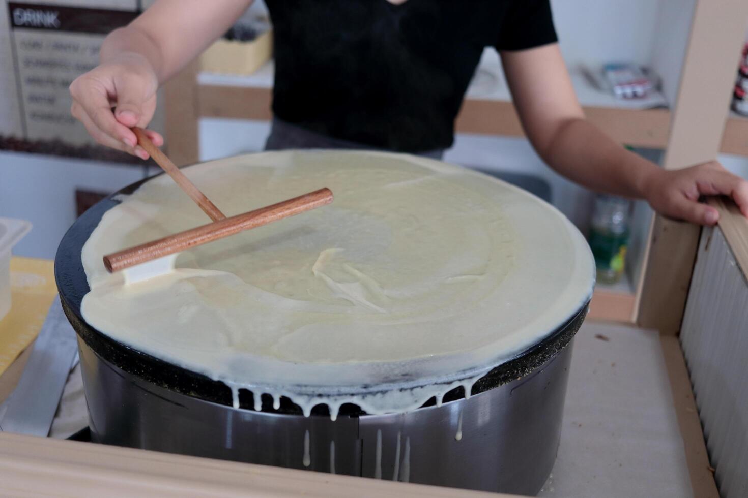 Crepe dough spreading on metal hot plate, woman making crepe sheet. photo