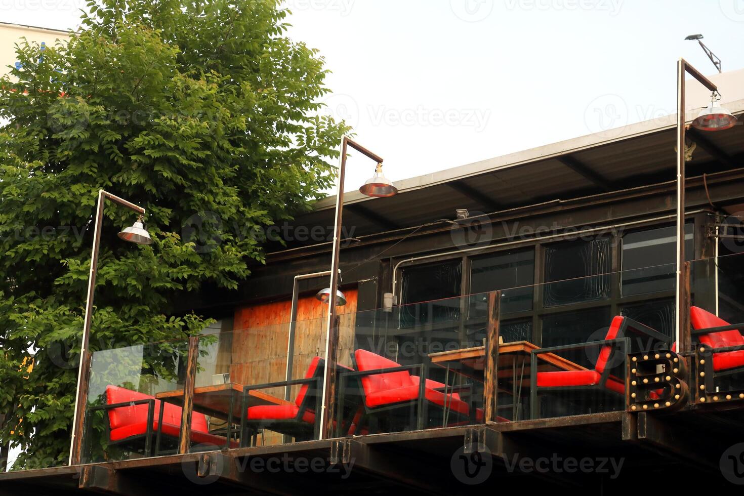 Bright red chairs and tables on large outdoor balcony of second floor wood house with glass fence. photo