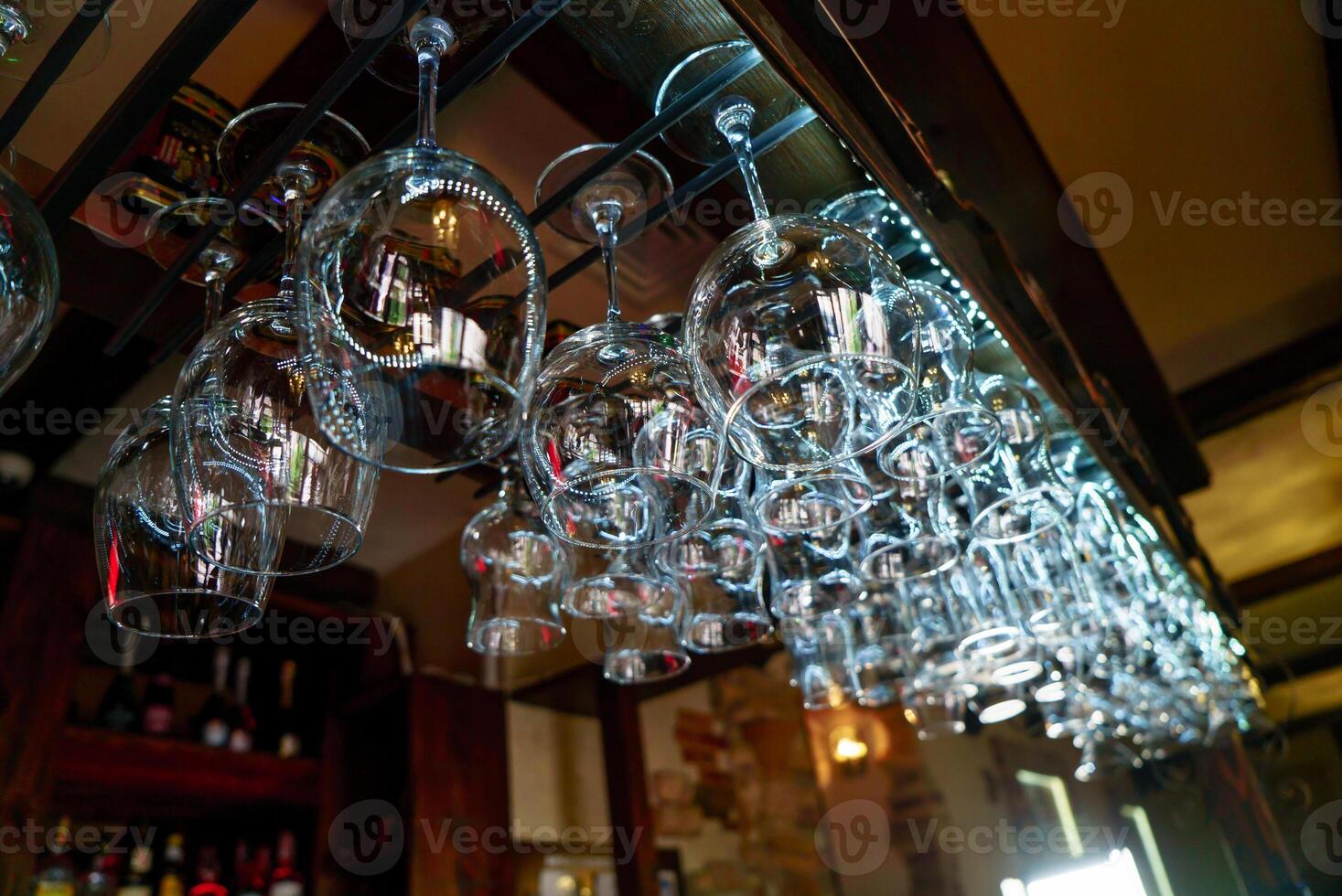 cristal vacío vino lentes colgando en el antecedentes de un bar encimera. limpiar vino lentes preparado por barman y colgado en el bar a un restaurante. foto