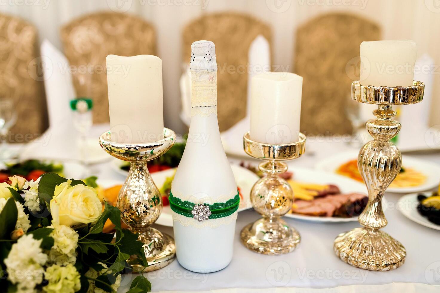 Festive table for guests, decorated with white candles, a bottle and the bouquet of flowers. Wedding banquet. photo