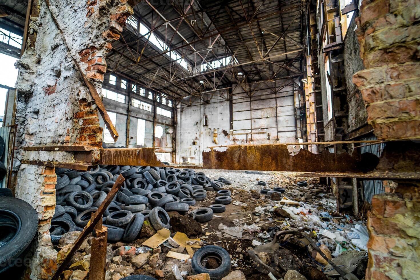 Destroyed old factory with garbage and a pile of used rubber tyres inside. Tires that are no longer suitable for use on vehicles in a damaged plant. photo