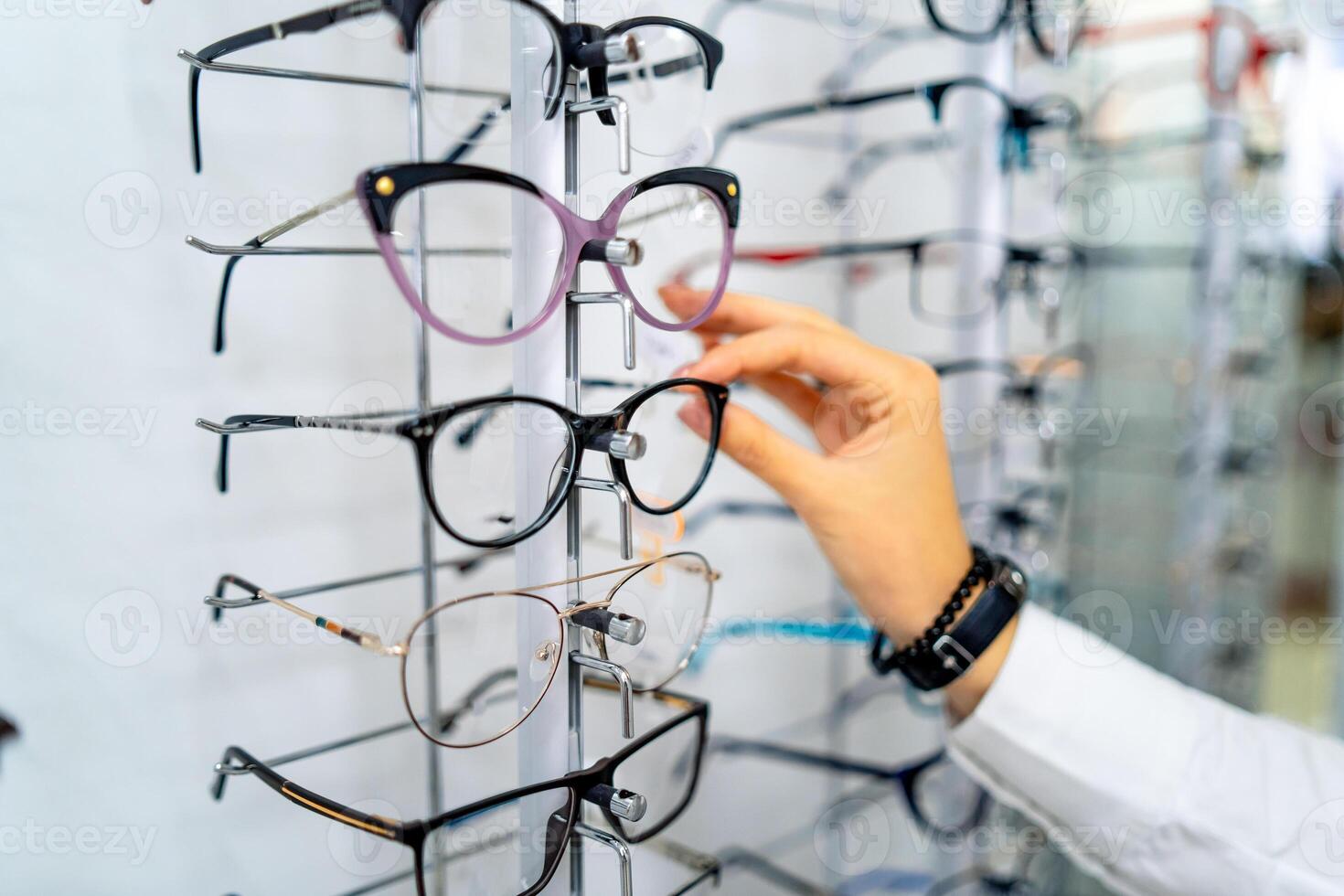 Row of glasses at an opticians. Eyeglasses shop. Stand with glasses in the store of optics. Woman's hand choosing glasses. Presenting spectacles. photo