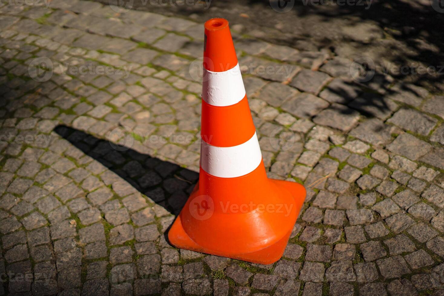 Close-up of striped orange and white road cone on pavement. Bright orange traffic cone for parking in the street. photo