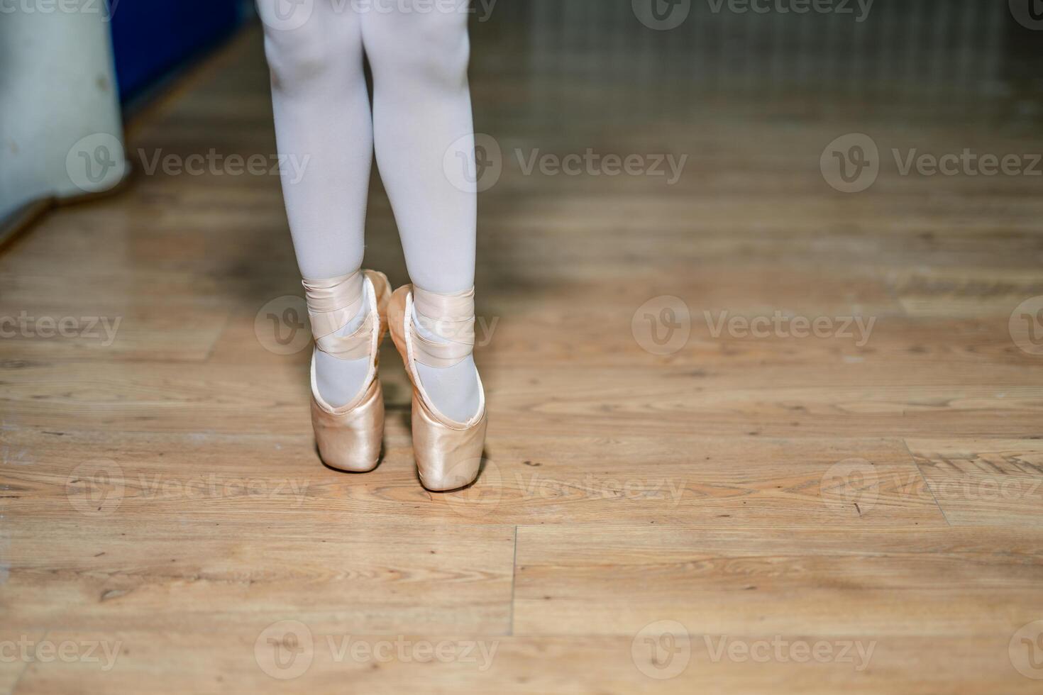 Legs of a little ballerina in a gold ballet shoes and white socks posing tiptoe in ballet hall on the floor. Closeup. photo