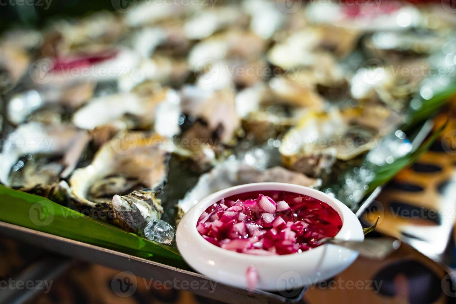 Bowl of traditional vinaigrette sause with freshly opened oysters on ice. Oysters in ice and a bowl of chopped onion. Healthy seafood. photo