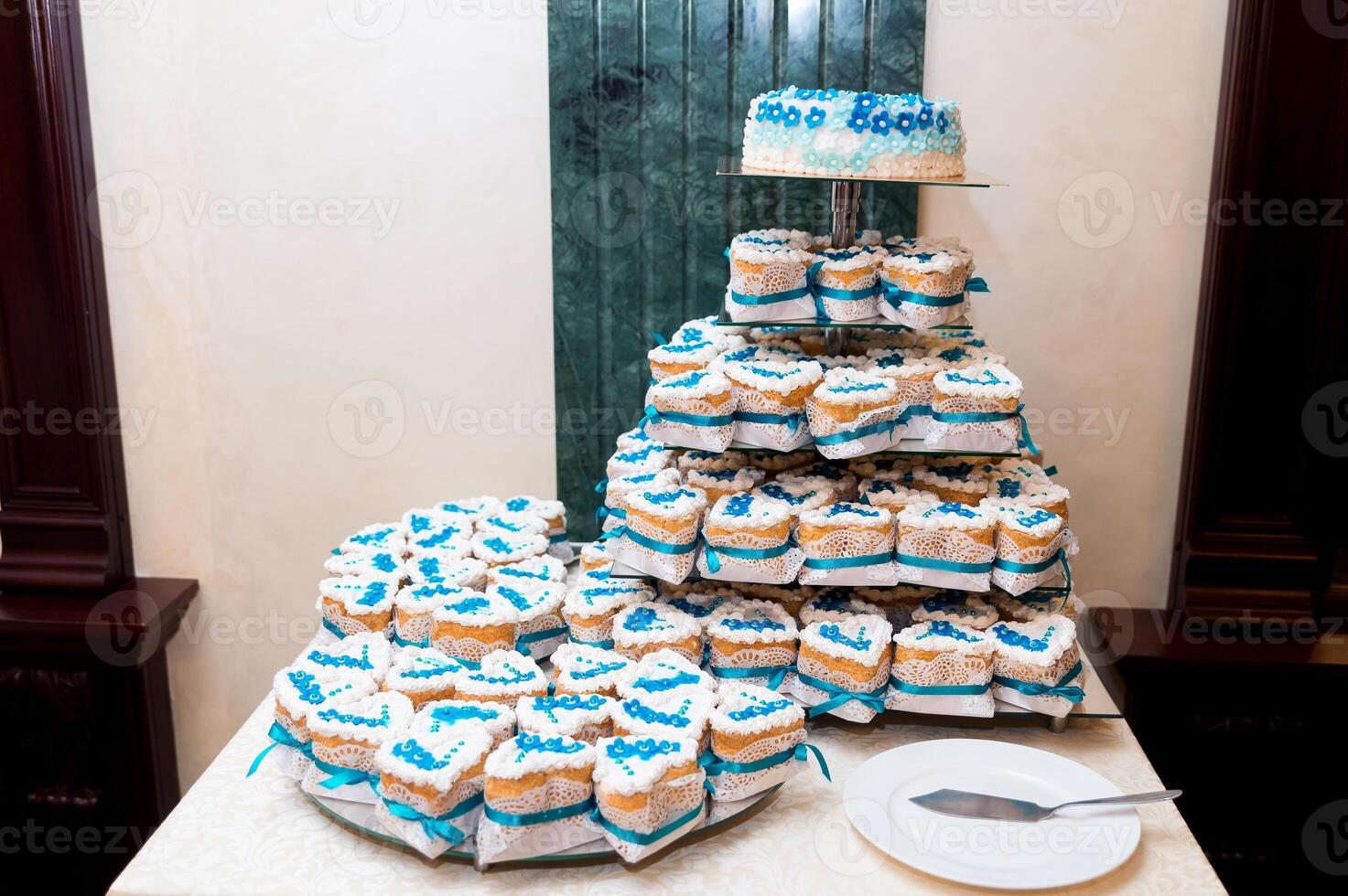 Wedding banquet decoration on the table with white tablecloth. Stylish candy bar with tasty cakes in white and blue colors. Cake stand assortment photo
