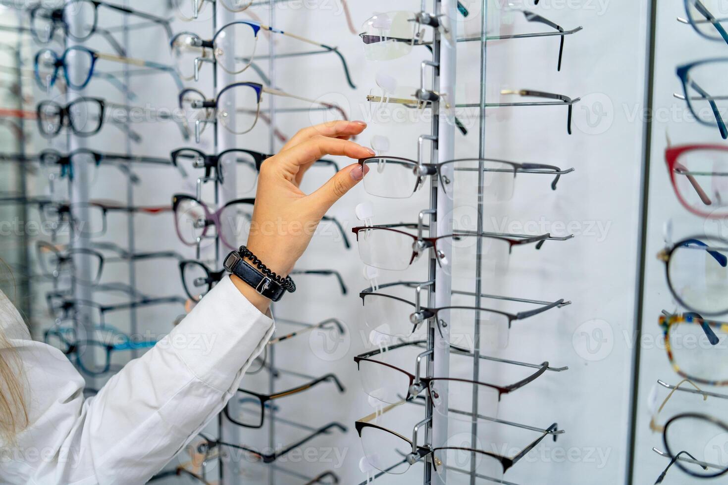 Row of glasses at an opticians. Eyeglasses shop. Stand with glasses in the store of optics. Woman's hand choosing glasses. Presenting spectacles. photo