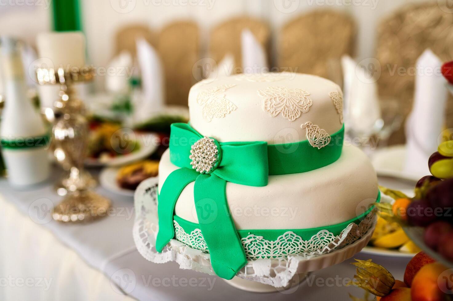 Delicious white cake in the form of a hat with green ribbon and a bow on the table background. Festive wedding table in the restaurant. Close-up photo