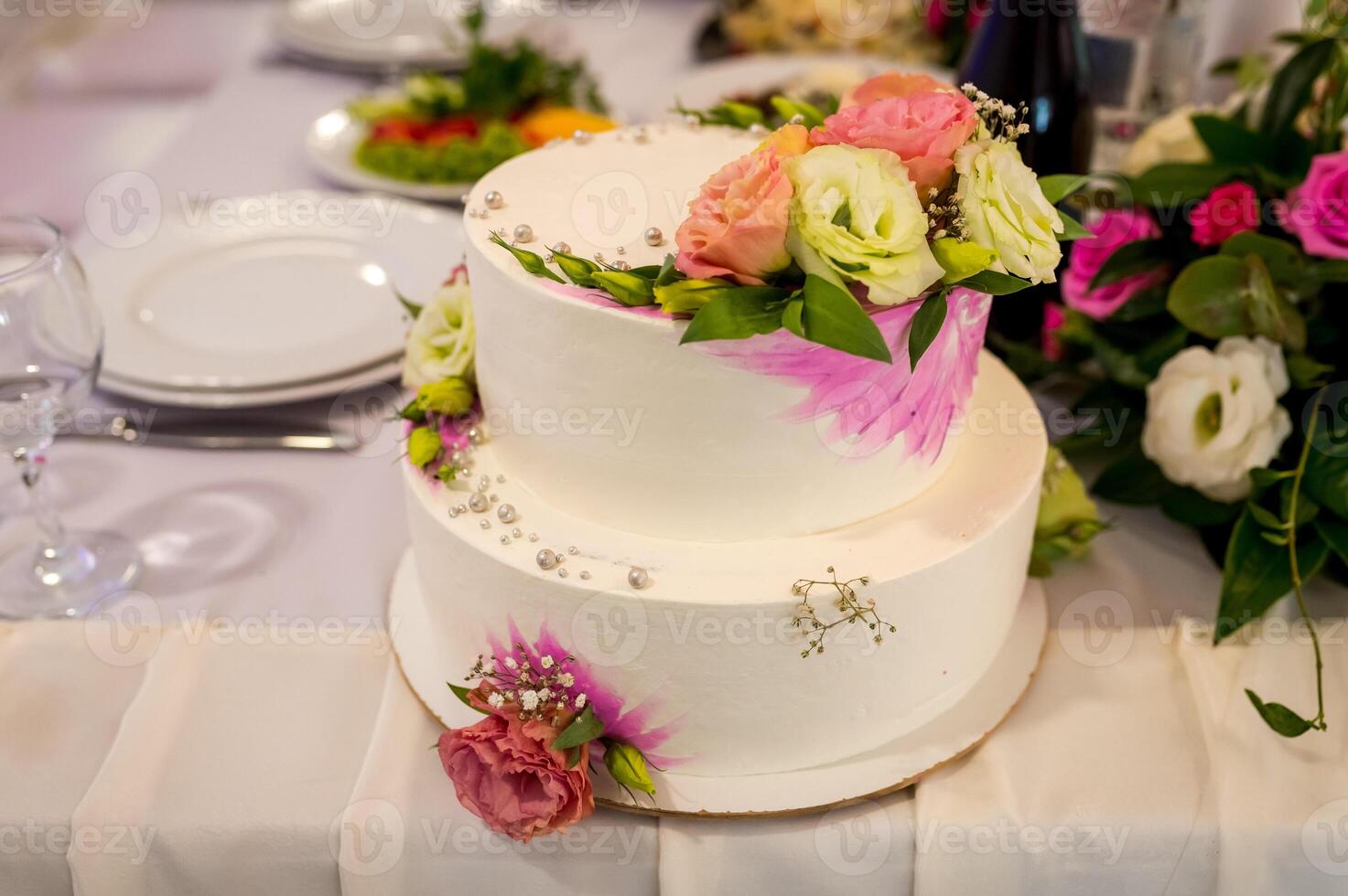 White Wedding Cake on a table with flowers on the background. Roses on a cake. photo