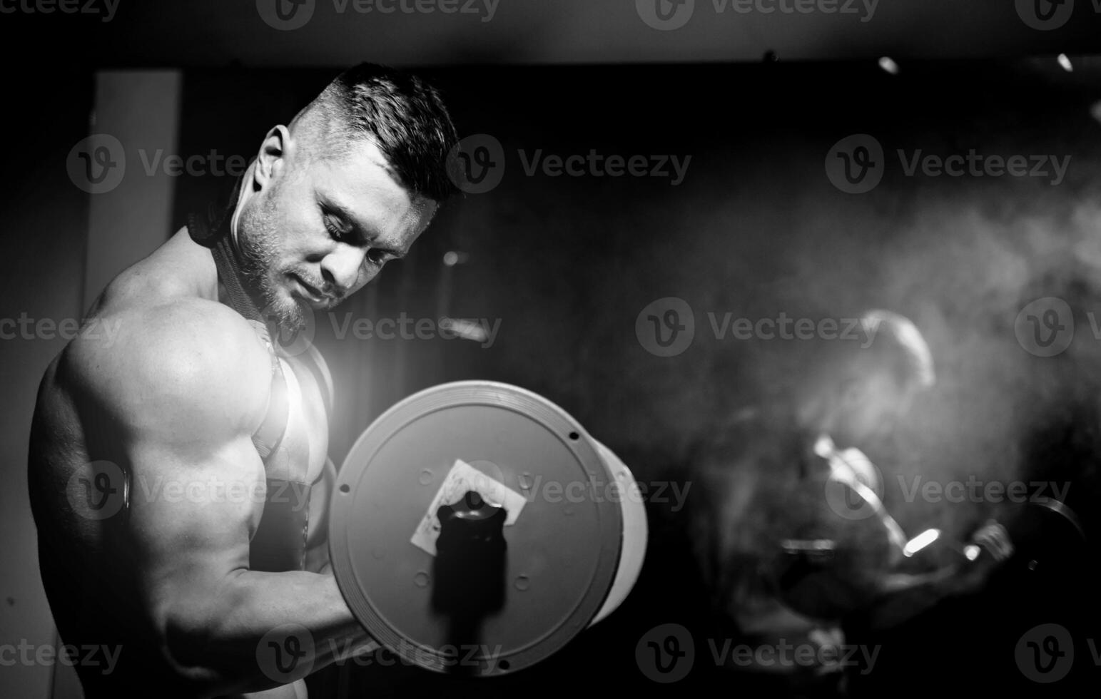 Handsome brutal sexy strong bodybuilder athletic fitness man pumping up muscles and lifting barbell. Bodybuilding concept. Black and white photo. View from the side closeup. photo