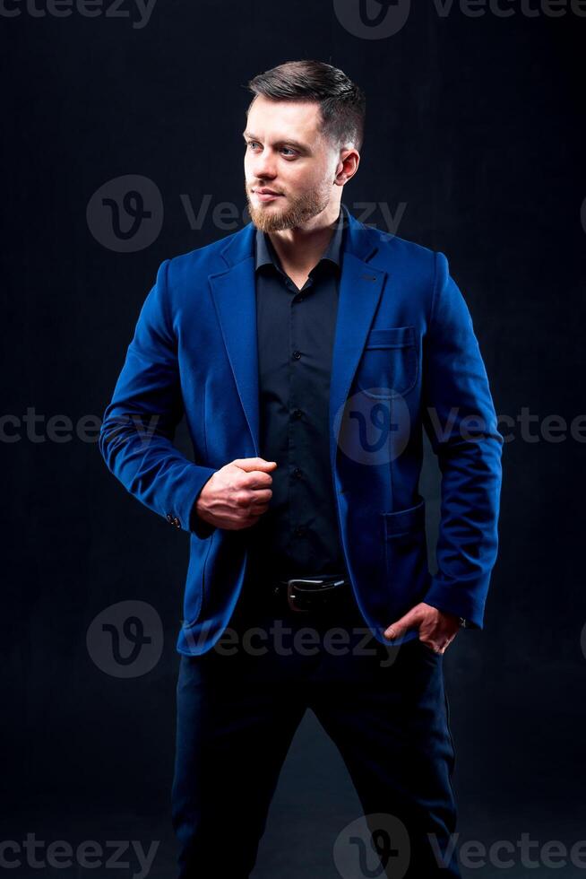 Portrait of european unshaven businessman dressed in formal suit posing and looking aside isolated over black wall photo