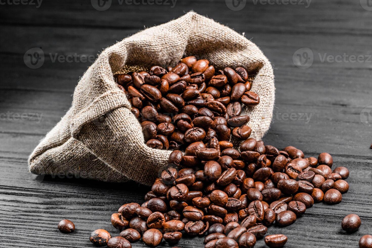 Sack full of aroma coffee beans pouring on the table. Fresh roasted arabica grains isolated on the wooden surface. Close-up photo