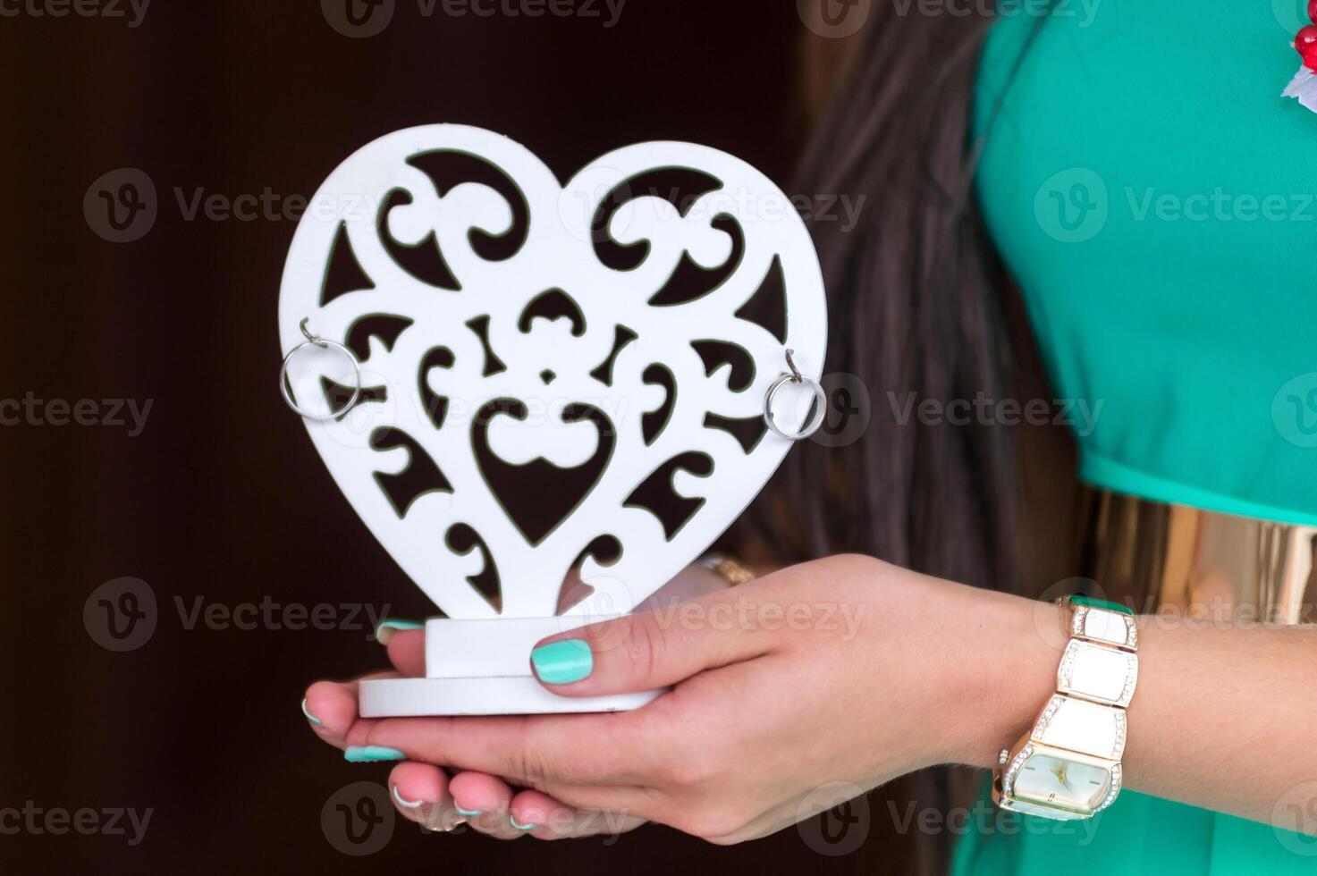 Wedding decor. Wooden vintage heart with golden rings on it in female hands. Closeup. photo