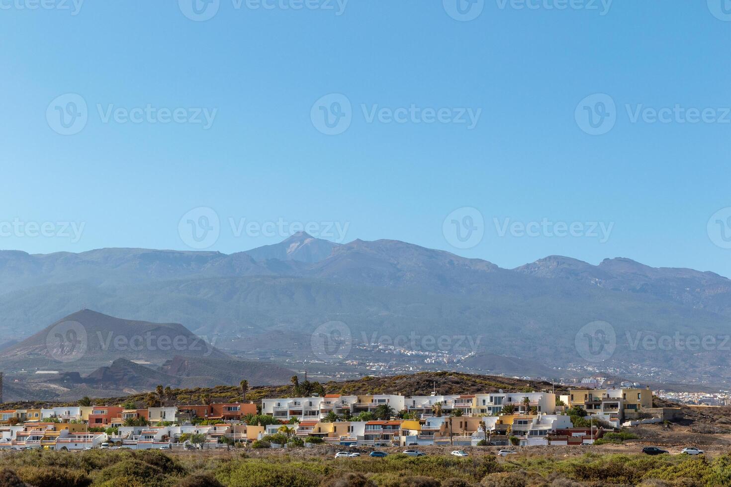 Scenic view of a tranquil town with white buildings nestled at the foot of a mountain range under a clear blue sky in Tenerife. photo