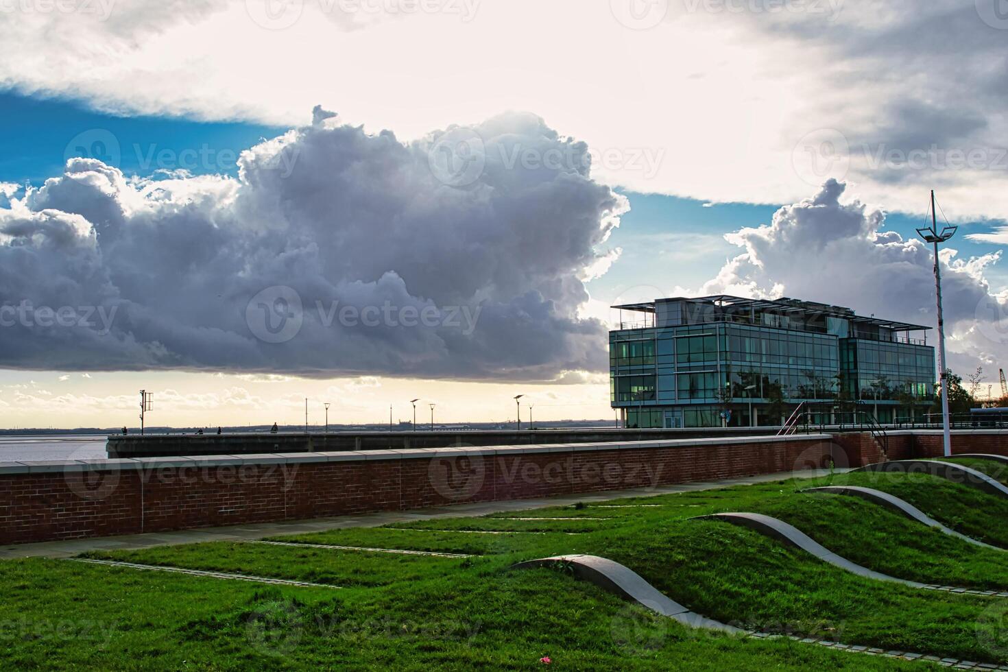 Modern building against a dramatic sky with sunbeams, green grass in the foreground and wavy landscape design. photo