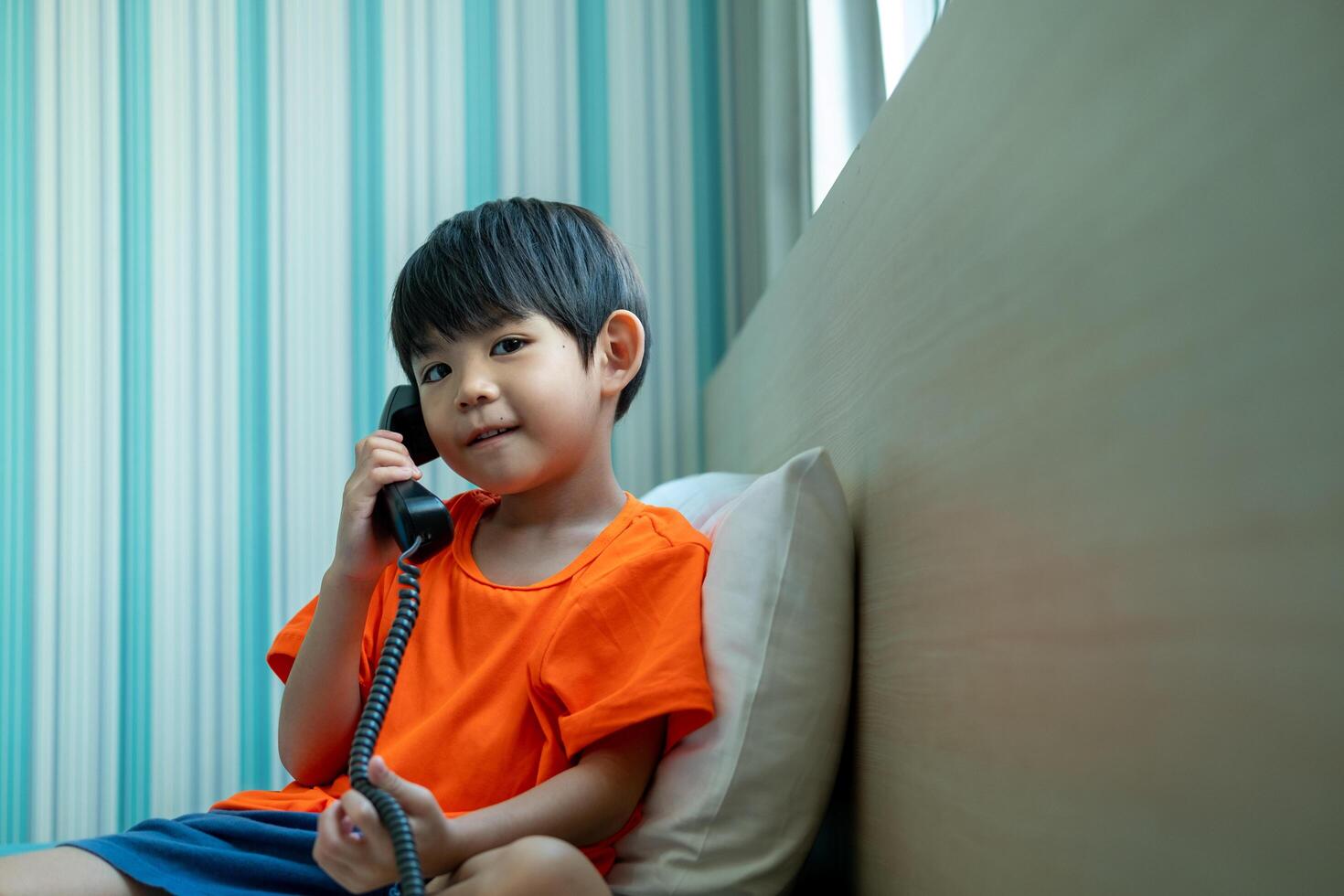 A little Asian boy lies on the bed talking on the phone. photo