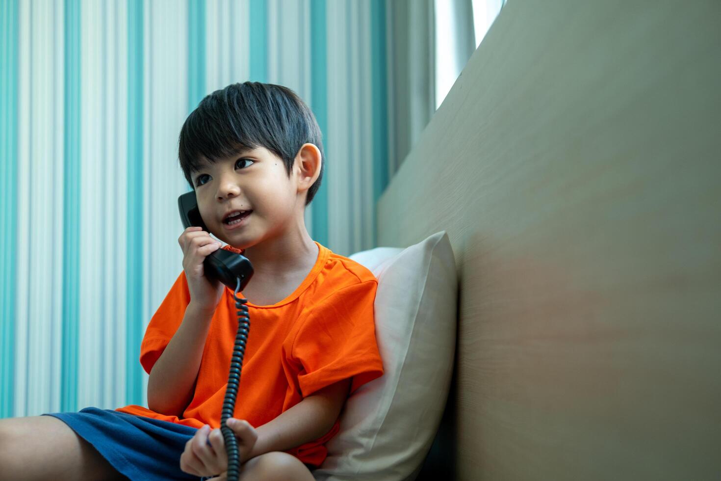 A little Asian boy lies on the bed talking on the phone. photo