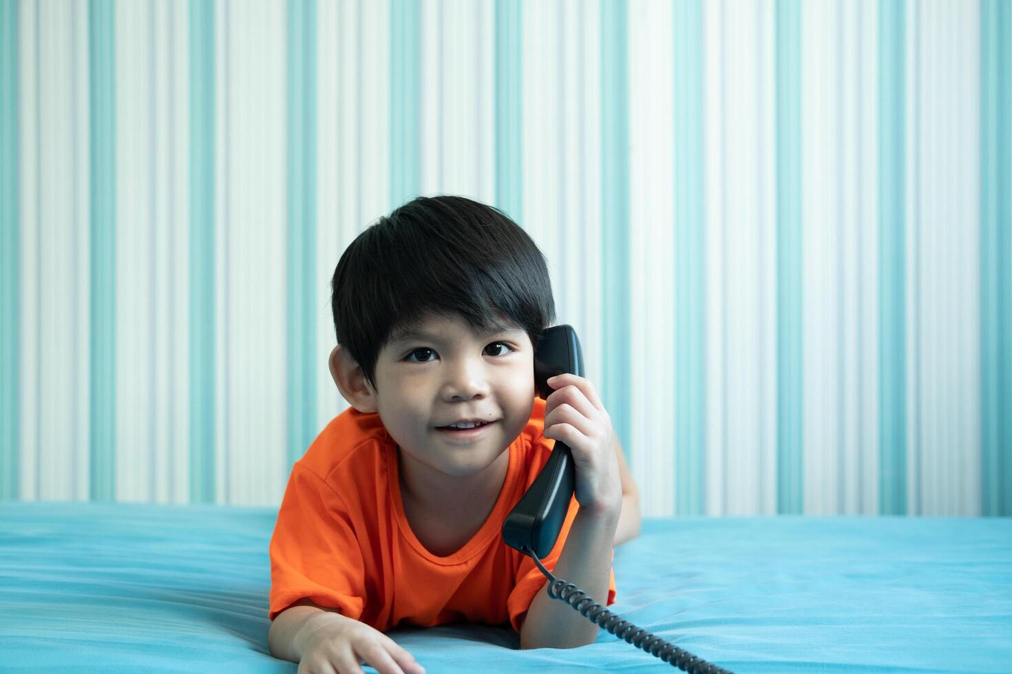 A little Asian boy lies on the bed talking on the phone. photo