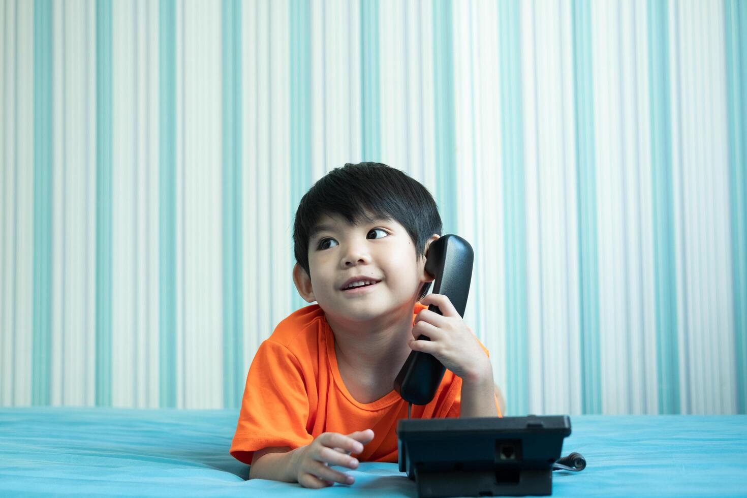 A little Asian boy lies on the bed talking on the phone. photo