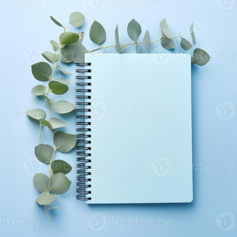 AI generated Elegantly designed blue paper notebook adorned with eucalyptus leaves on a serene blue background. Ai Generated photo