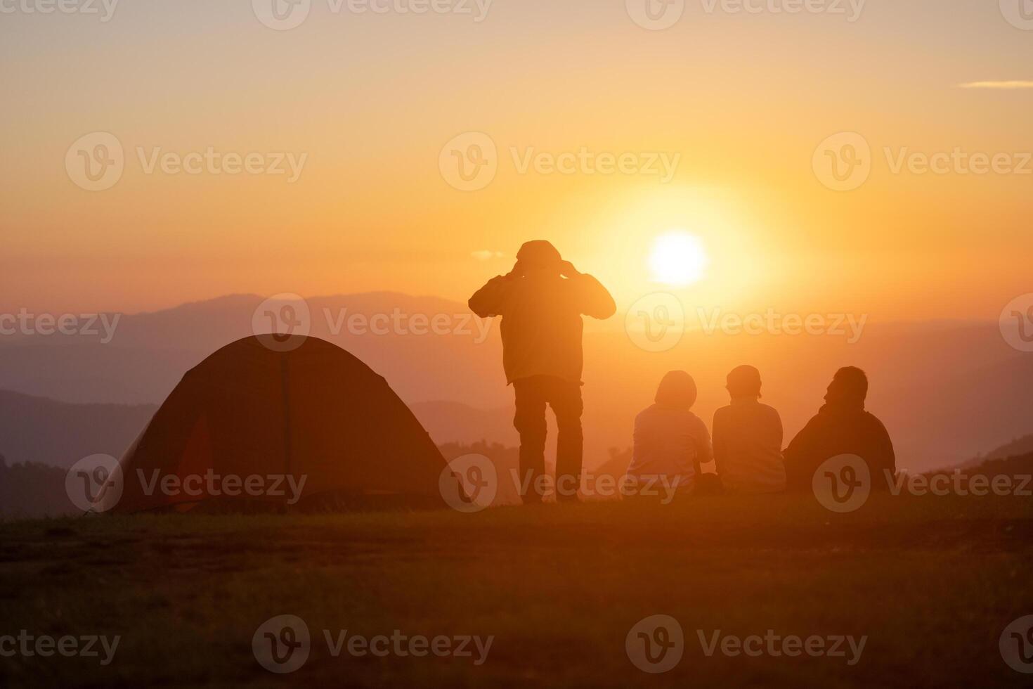 grupo de amigos sentado por el tienda durante durante la noche cámping mientras mirando a el hermosa ver punto puesta de sol terminado el montaña para al aire libre aventuras vacaciones viaje concepto foto