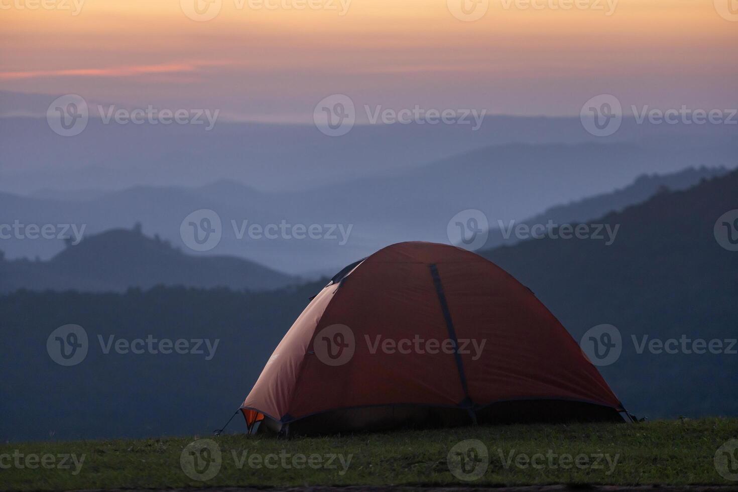 Adventurer tents during overnight camping site at the beautiful scenic sunset view point over layer of mountain for outdoor adventure vacation travel concept photo