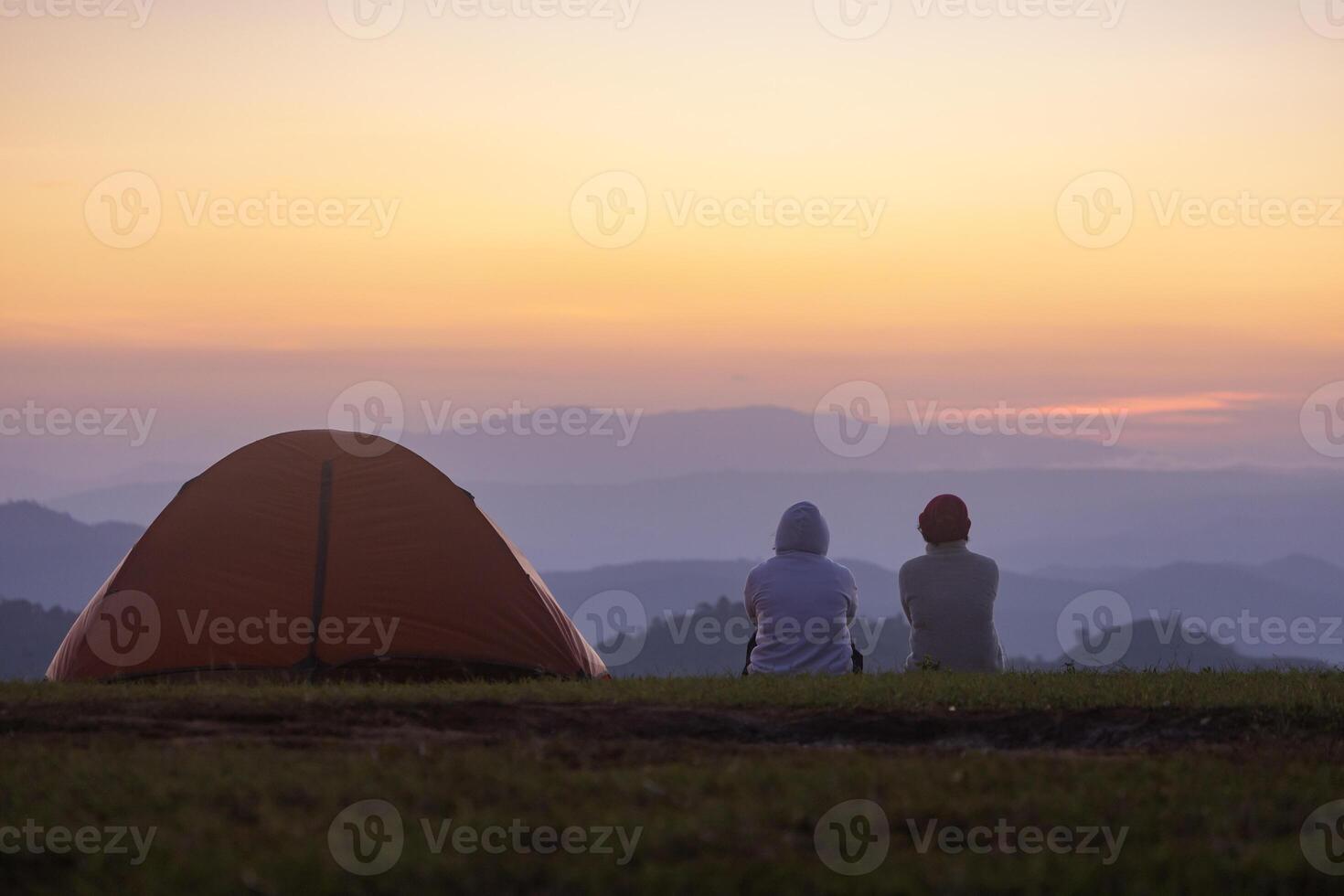 Couple is sitting by the tent during overnight camping while looking at the beautiful scenic sunset over the mountain for outdoor adventure vacation travel concept photo
