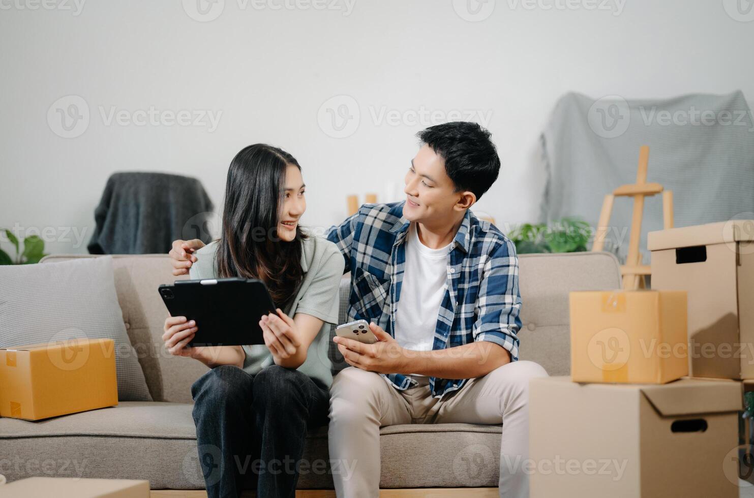 joven Pareja con grande cajas Moviente dentro un nuevo casa, nuevo Departamento para pareja, joven asiático hombre y mujer Ayudar a levantar cajas en sofá foto