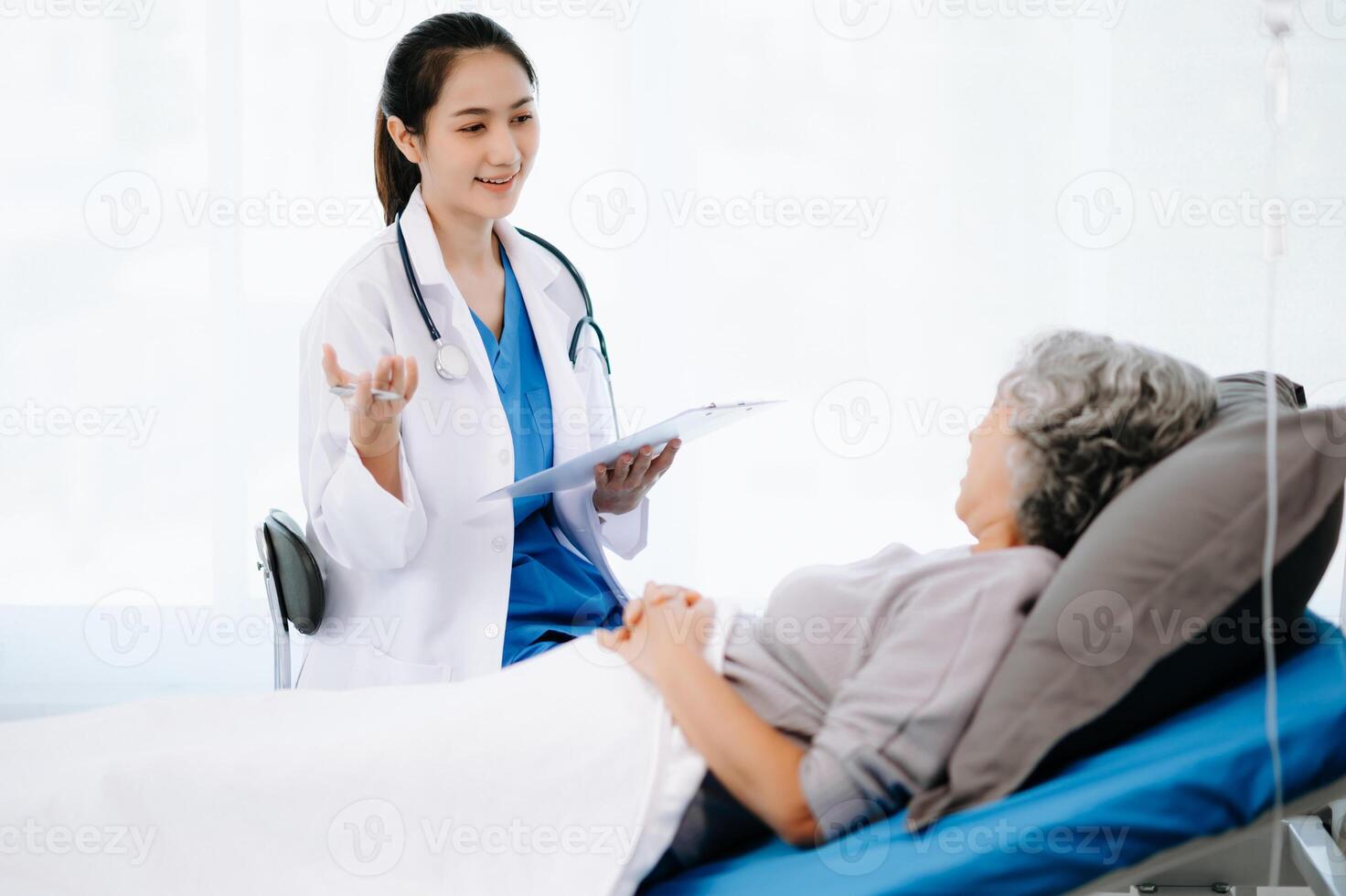 Doctor and Asian elderly patient who lie on the bed while checking pulse, consult and explain with nurse taking note in hospital wards. photo