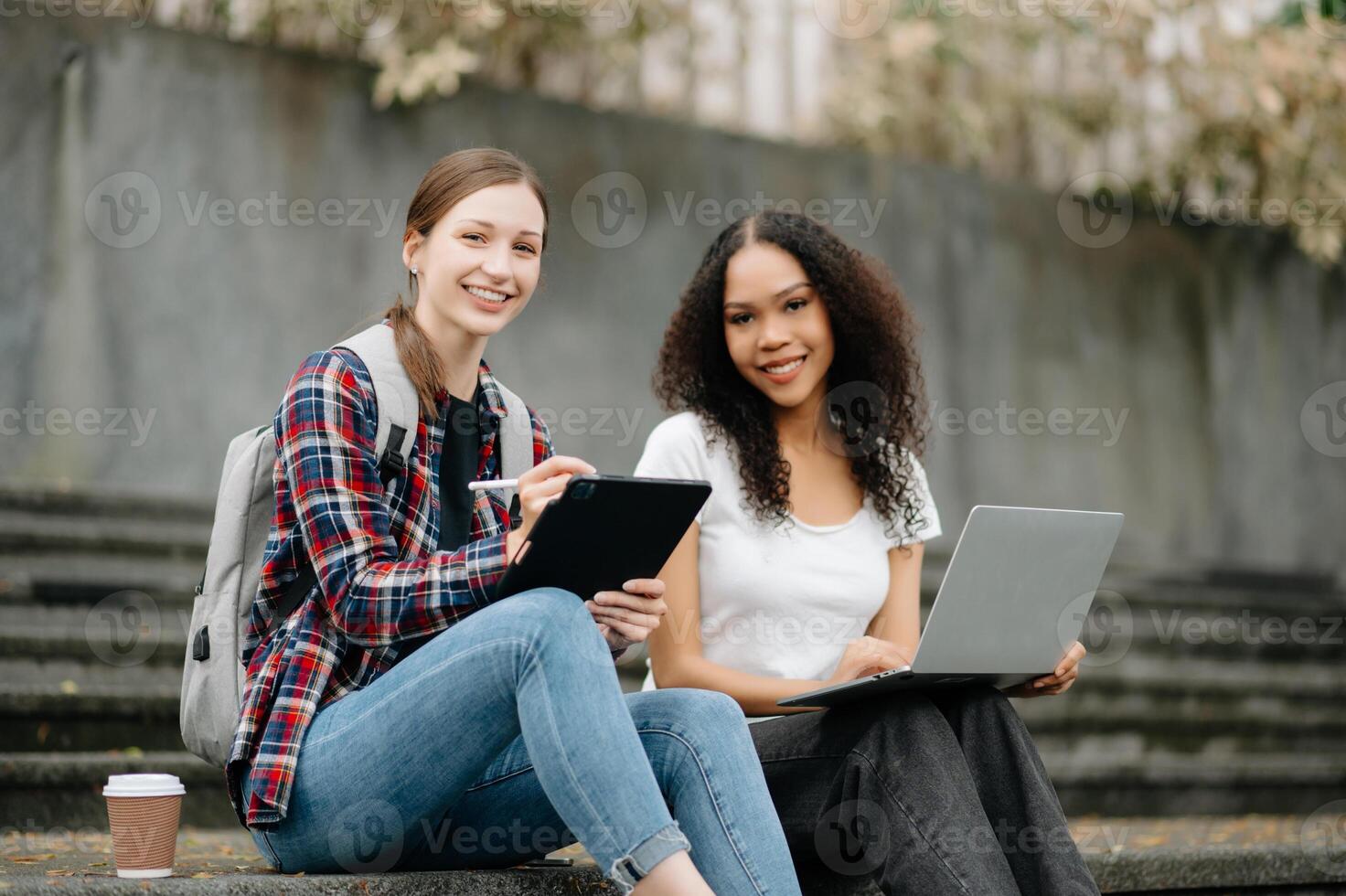 Young college students focusing on his school project, looking at laptop and tablet, discussing and working together at the campus park photo