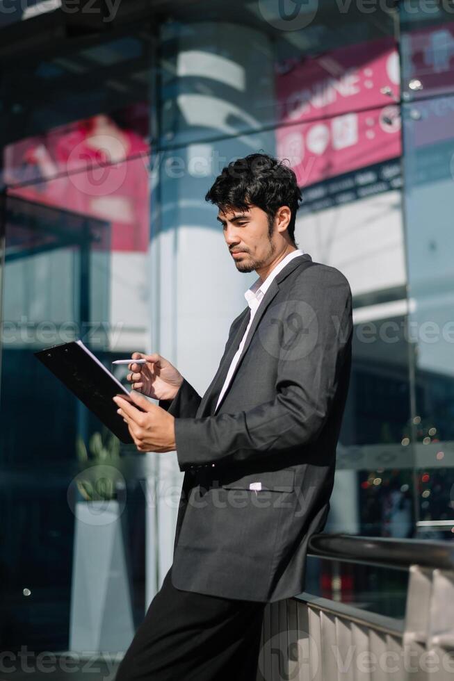 Businessman looks at smart phone reads news from phone and writes in messenger outside office photo