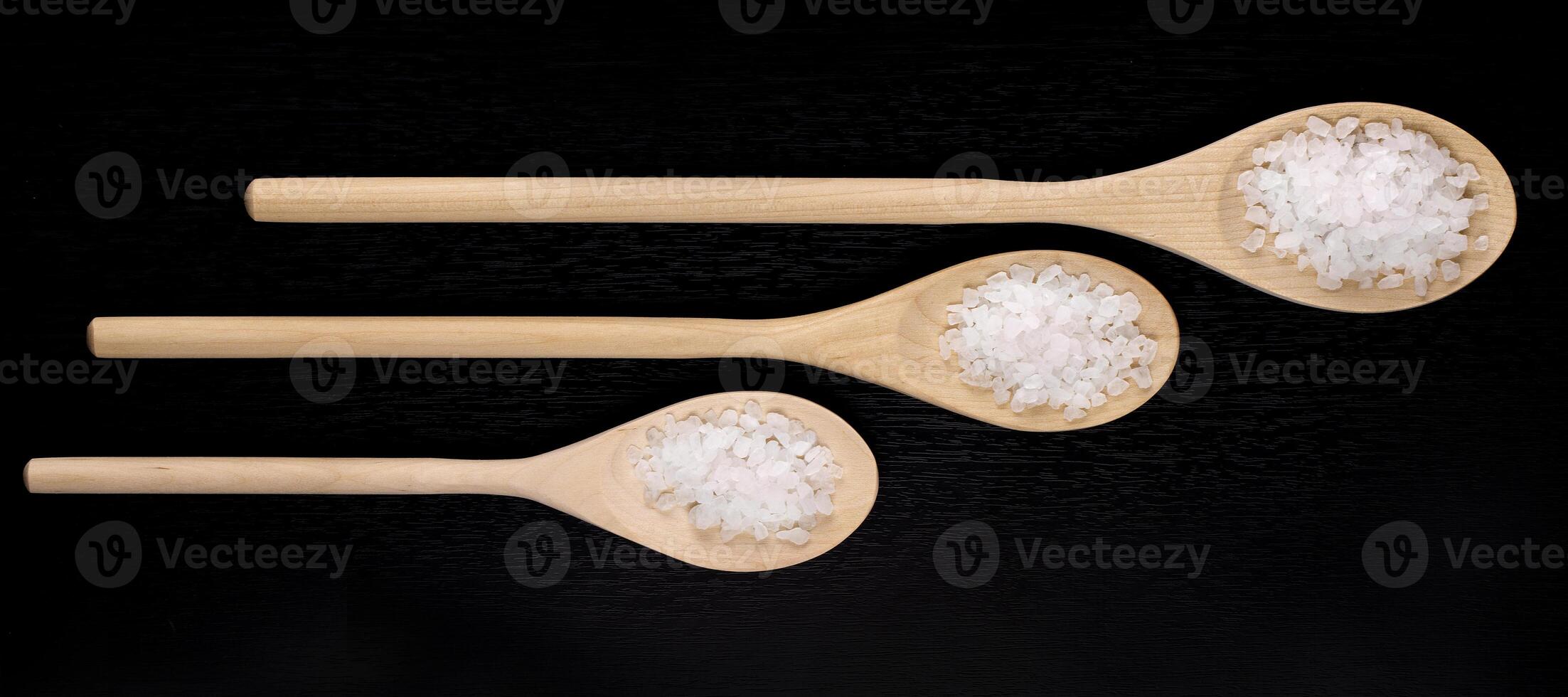 White sea bath salt in wooden spoons on a dark polished table photo