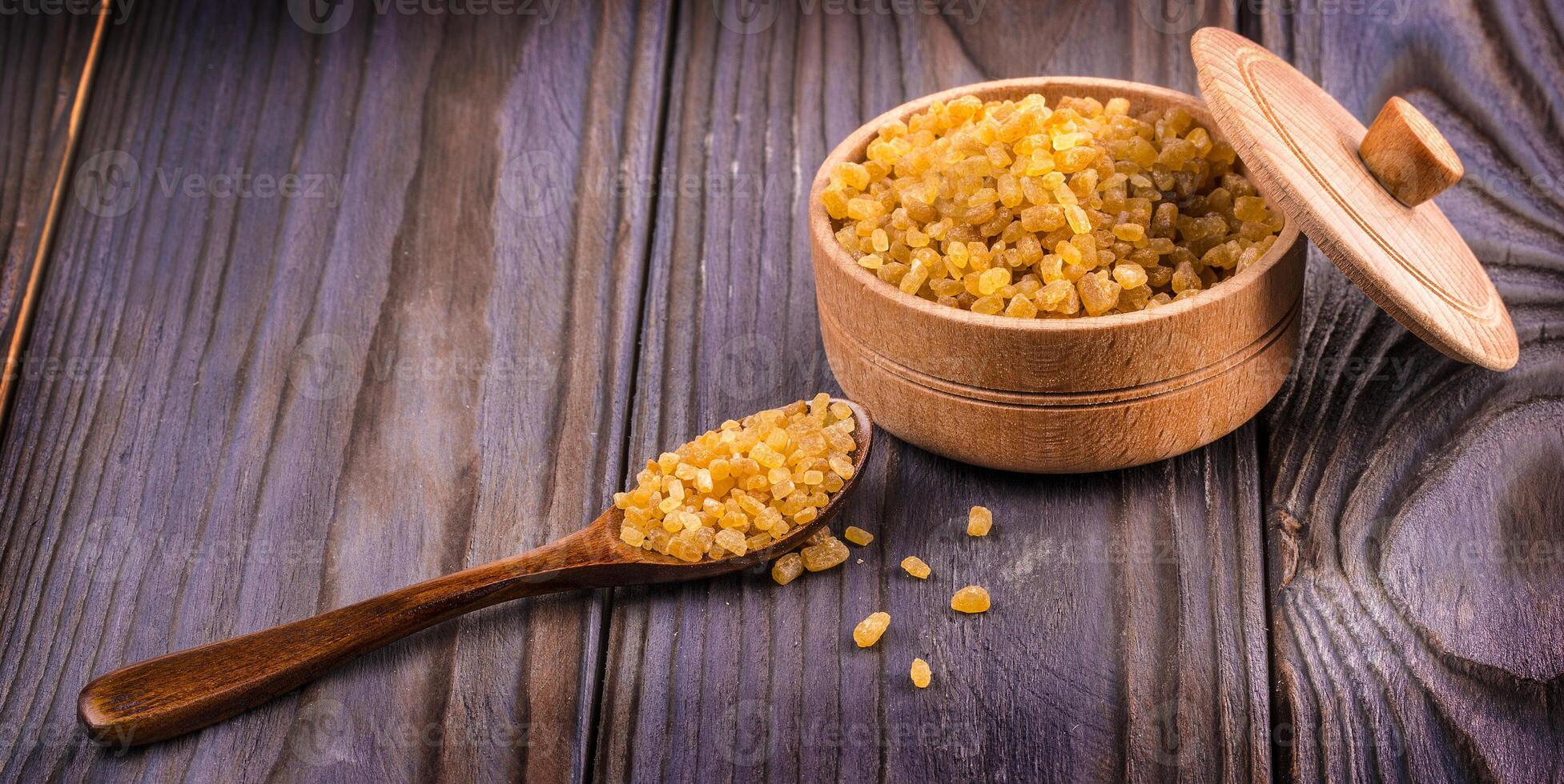 The Wooden scoop spoon and bowl full of brown cane sugar with pinch of sugar spilled around on wooden table, top view photo